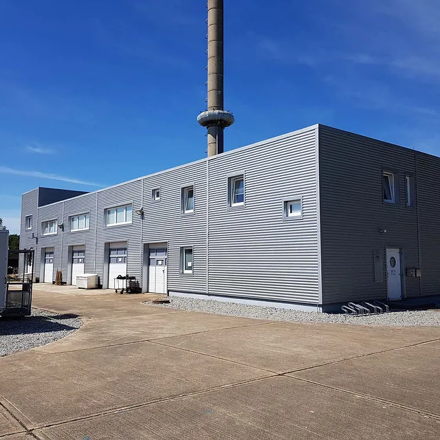 Großes Industriegebäude mit Metallfassade und Schornstein auf einem Betriebsgelände für technische Spezialarbeiten.